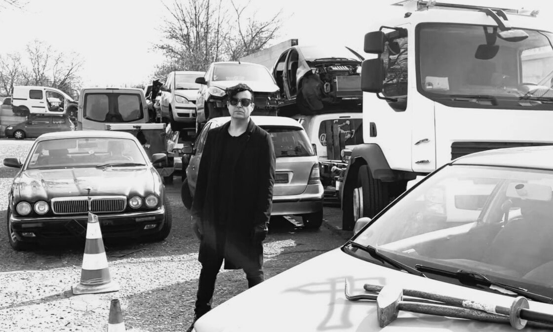 Das Bild zeigt den Musiker Janosch Moldau auf einem Schrottplatz für Autos.